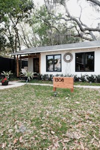 Charming single-story white house in Orlando featuring a well-maintained front yard with fallen leaves and lush greenery.
