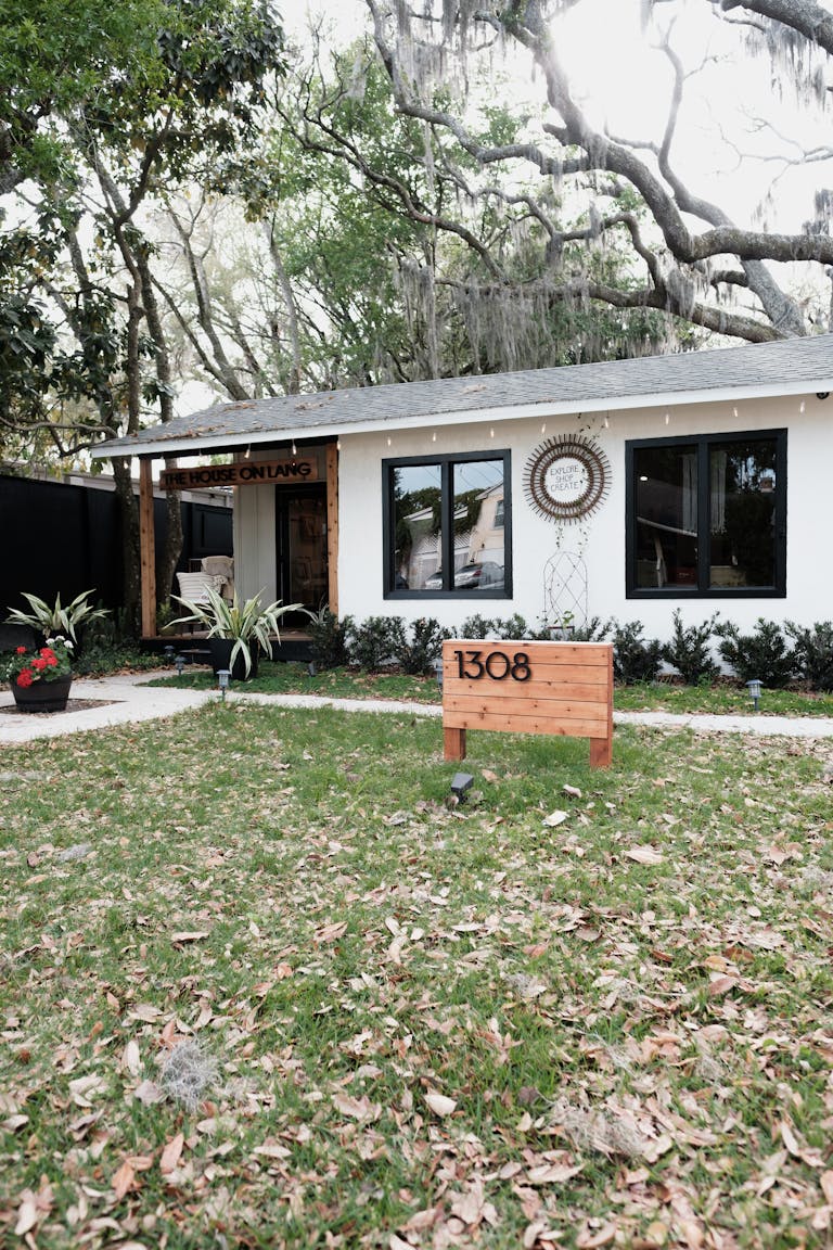 Charming single-story white house in Orlando featuring a well-maintained front yard with fallen leaves and lush greenery.