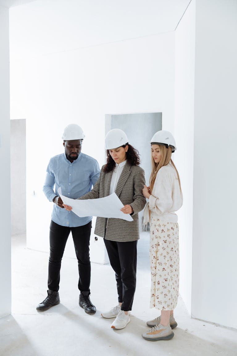 Three people in hard hats examining construction plans in a new home's interior.