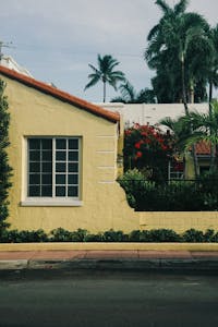 A charming yellow house with lush tropical plants and palm trees, evoking a warm, sunny vibe.