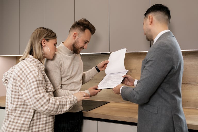 A couple reviews real estate documents with an agent in a modern indoor setting, discussing a potential property purchase.