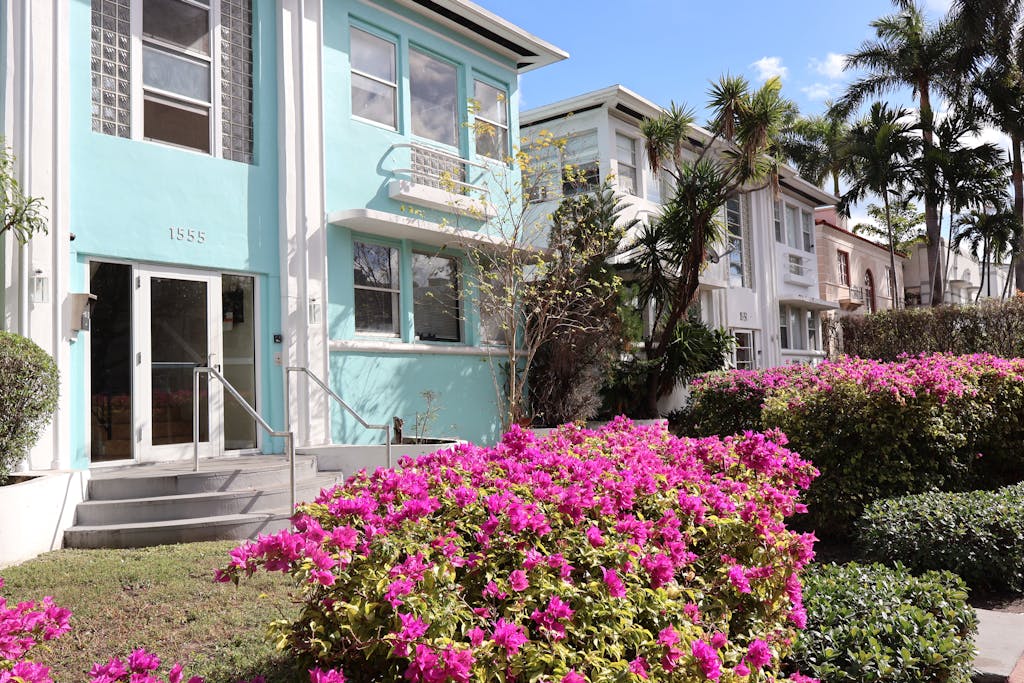 Charming pastel houses with vibrant pink azaleas and palm trees in a sunny setting.