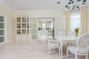 Interior of spacious light dining room with white table and cozy chairs near large window with curtains
