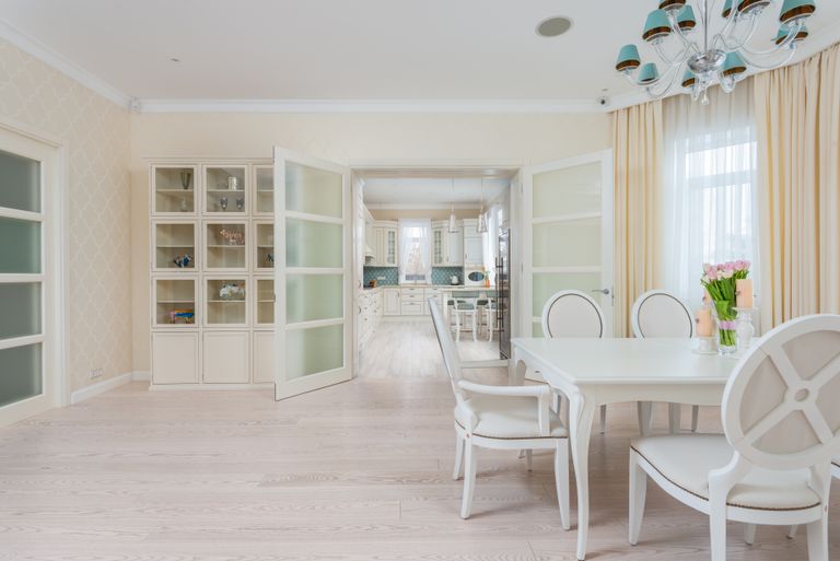 Interior of spacious light dining room with white table and cozy chairs near large window with curtains
