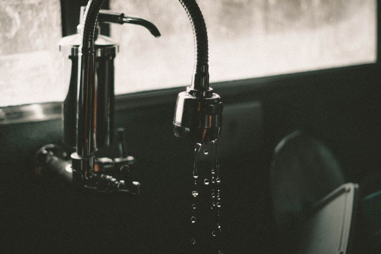 Close-up of a kitchen faucet with water droplets falling into the sink, captured in a minimalist style.