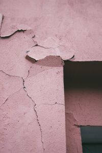 Detailed view of a cracked and weathered pink concrete wall with peeling paint.
