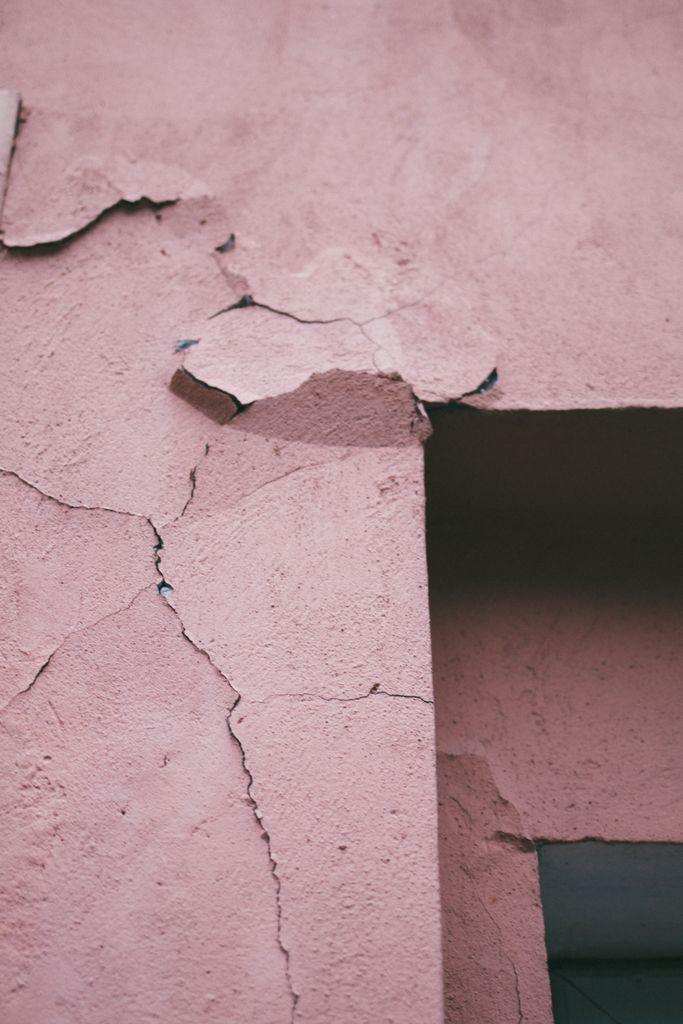 Detailed view of a cracked and weathered pink concrete wall with peeling paint.